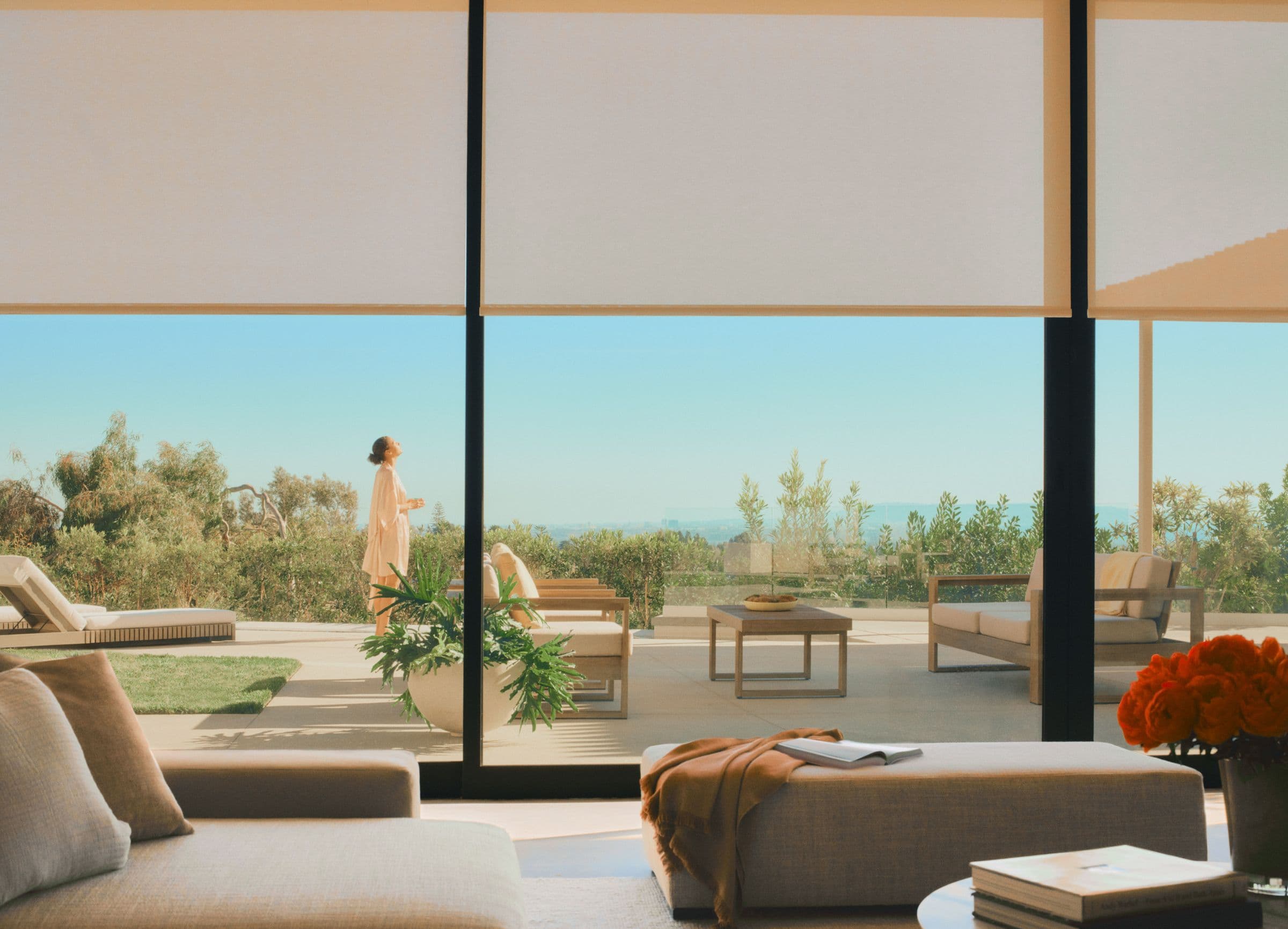 A wall of glass with light roller shades lowered a third of the way over a sunny patio