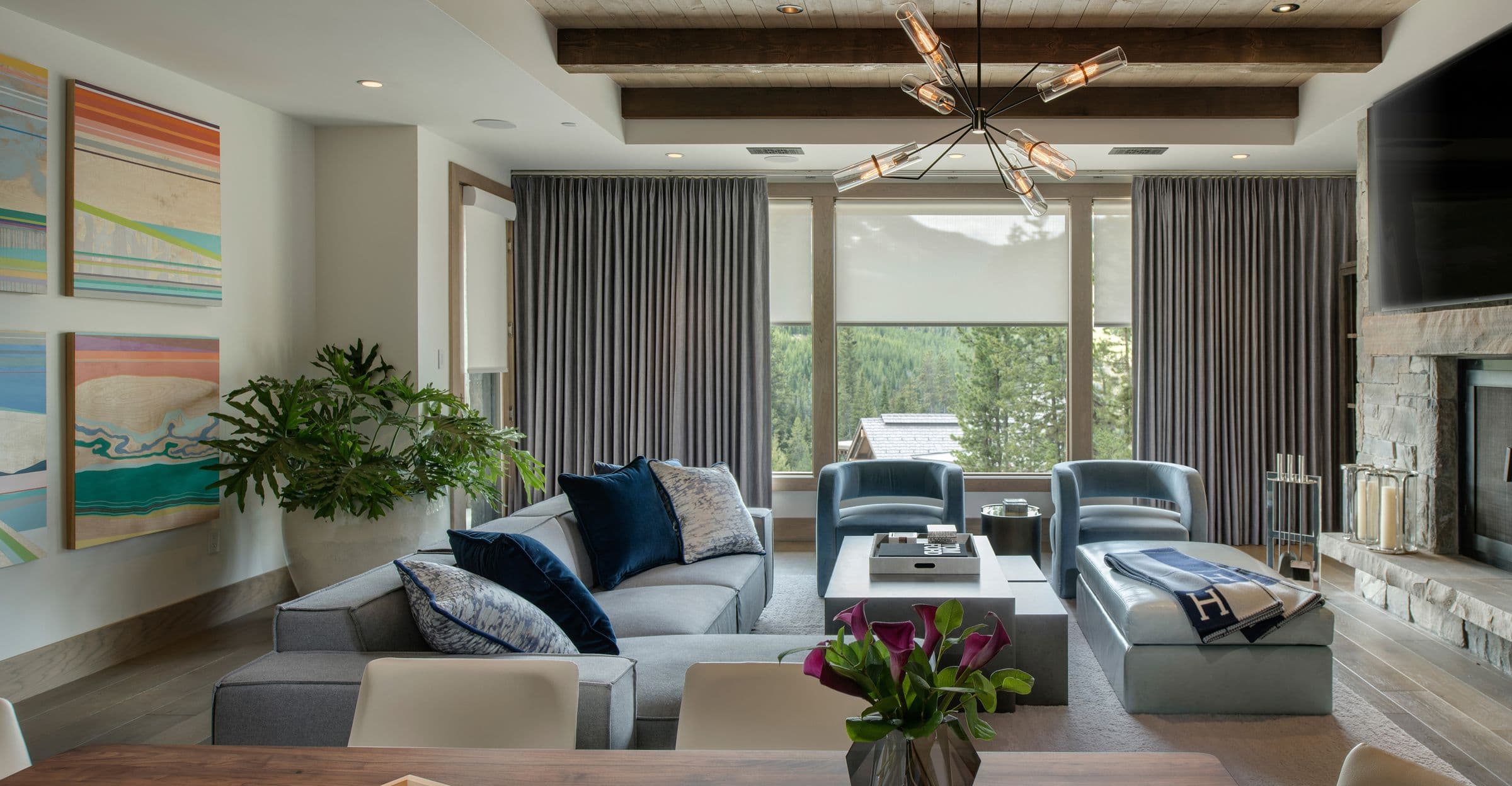 A mountain family room with a stone fireplace, gray drapery and white roller shades layered on the windows