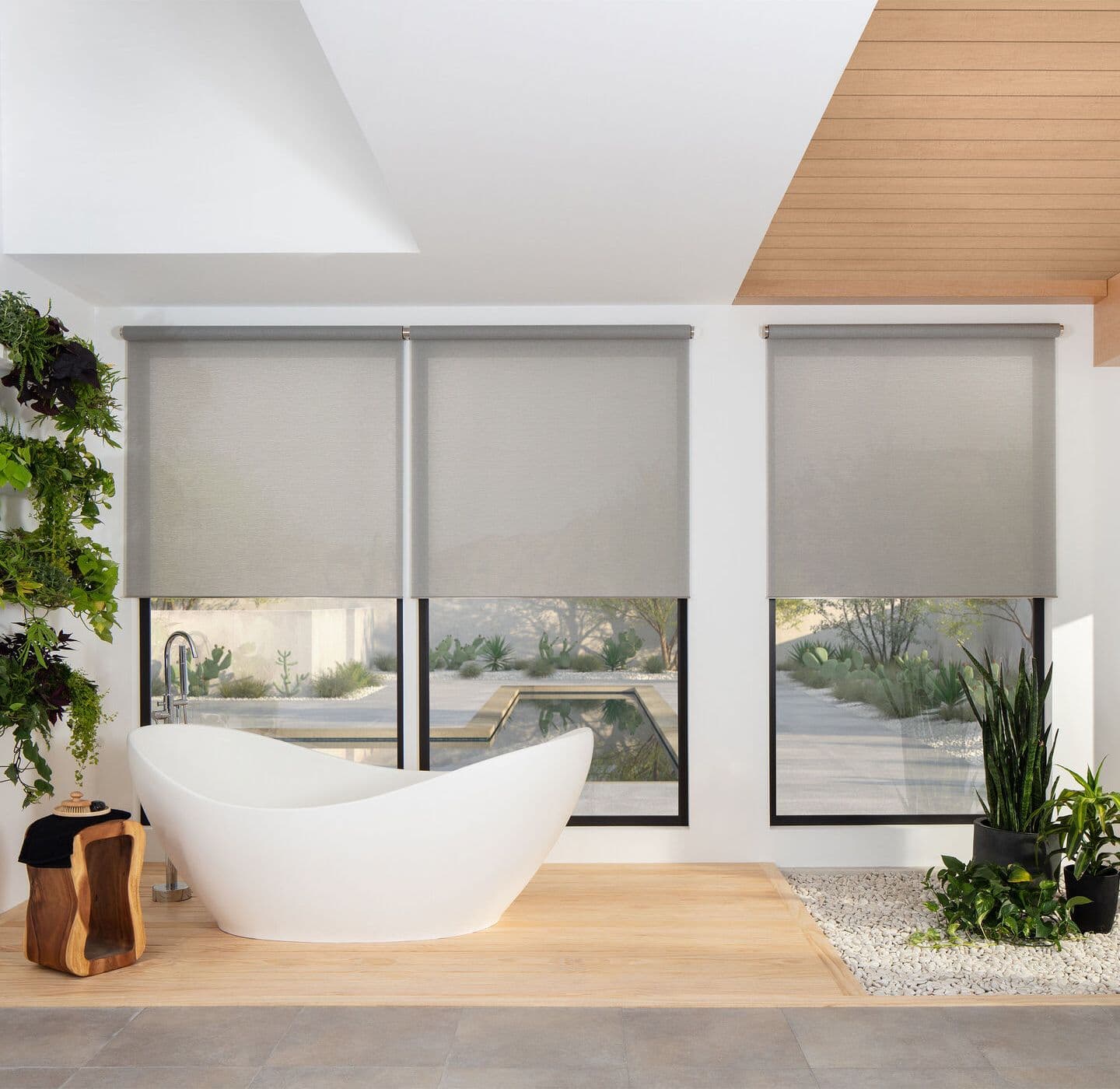 A spa bathroom with three open roll shades half lowered behind a freestanding tub