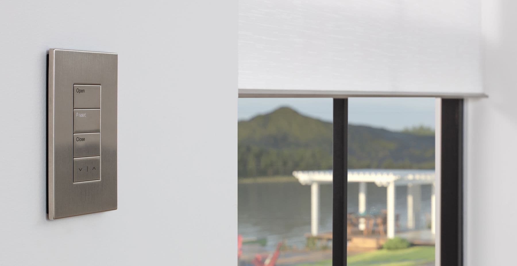 A brushed metal keypad engraved Open, Preset and Close beside a partly lowered shade