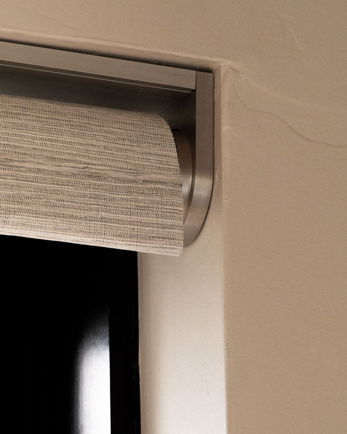 Close-up of a woven linen-look shade fabric rolled under a brushed aluminum channel