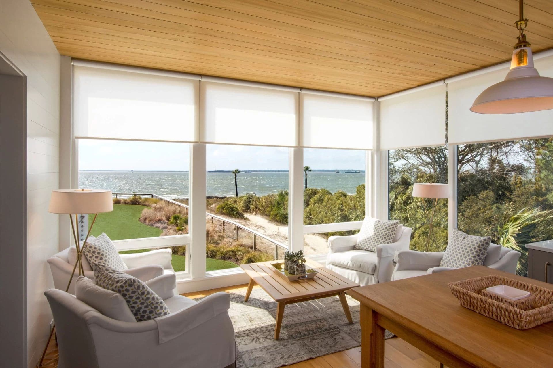 A bright sunroom with white light-filtering shades lowered a third of the way over a harbor view