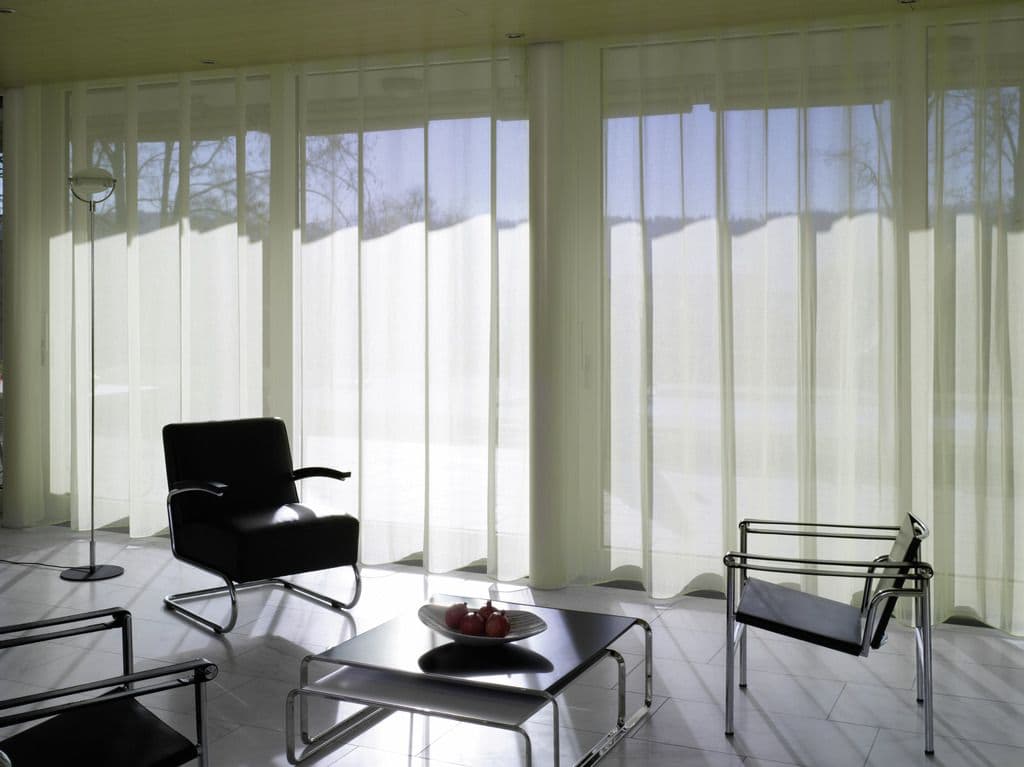 A long run of floor-to-ceiling glass covered by a sheer wave curtain on a motorized track