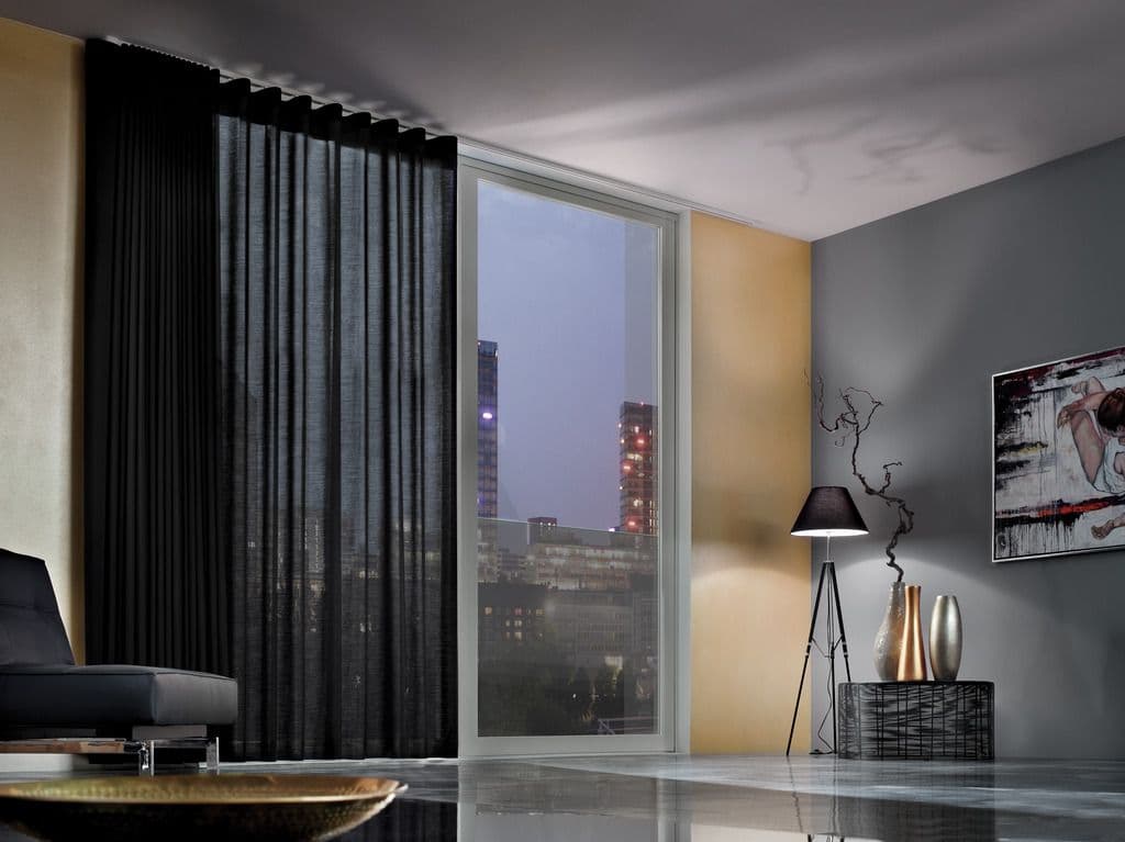 A black wave curtain stacked beside a tall glass door at dusk